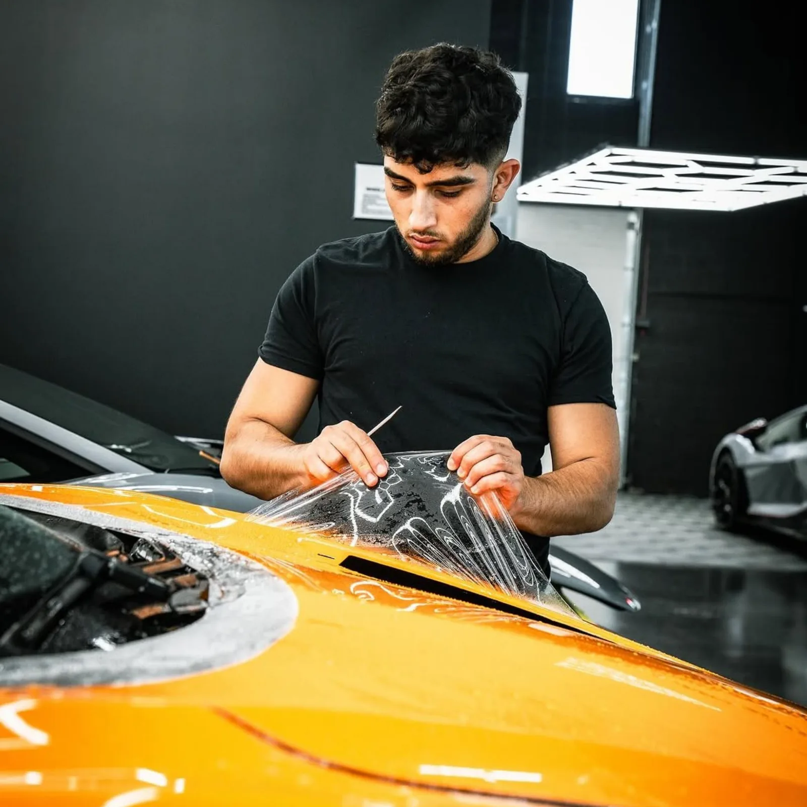 Paint protection film being trimmed on the bonnet of an orange supercar