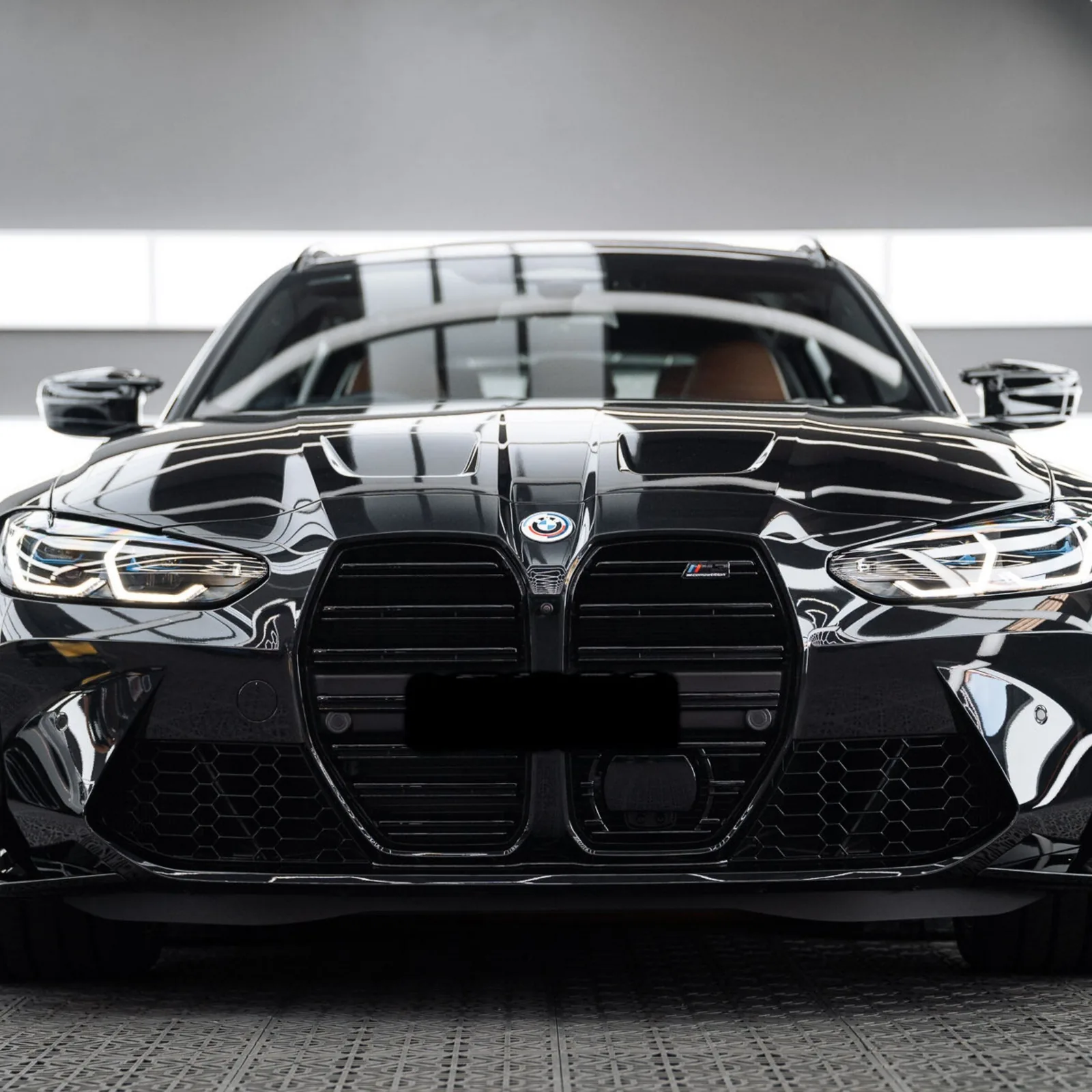 Front of a gloss black BMW M3 against a light studio wall